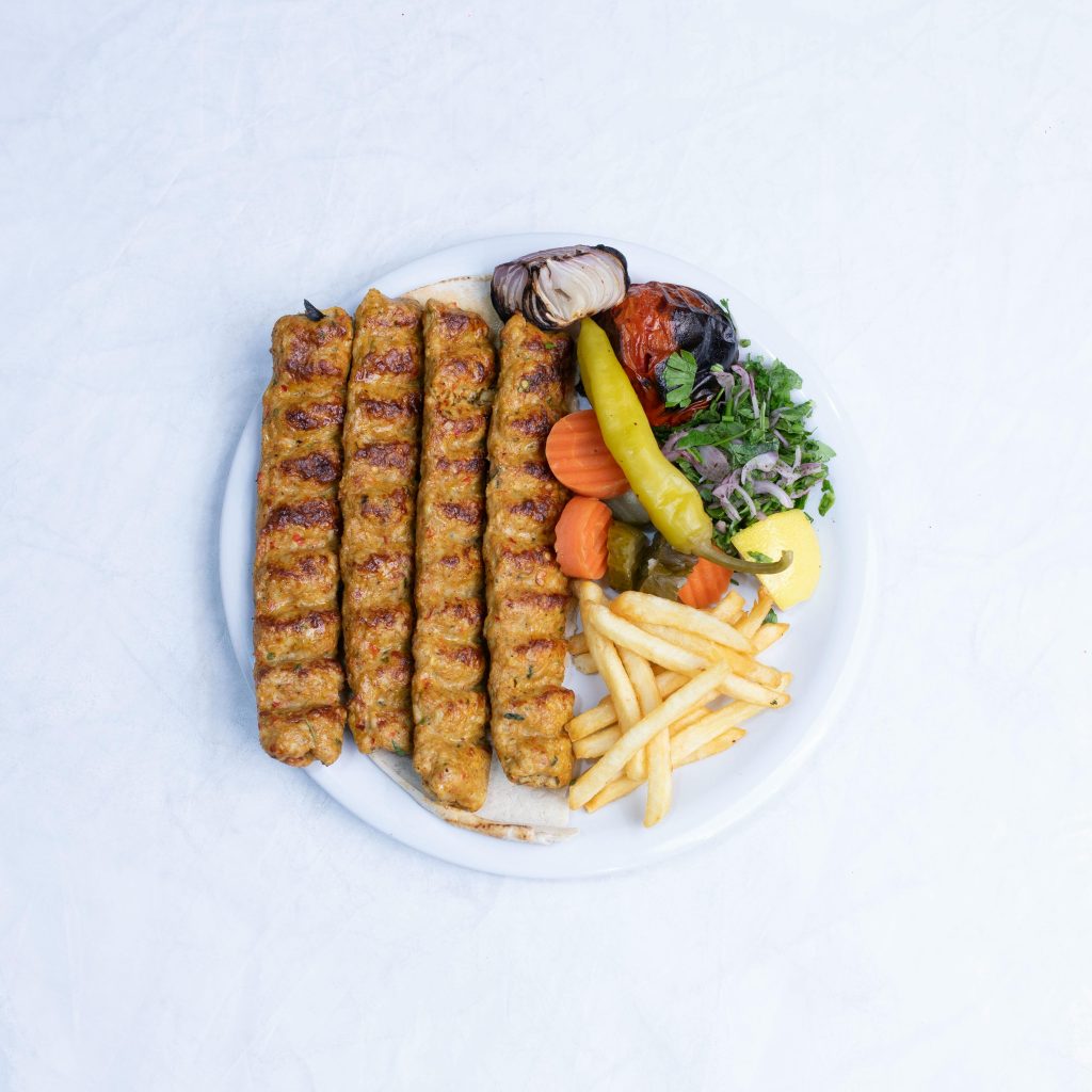 Appetizing grilled kebabs served with fries and fresh vegetables on a white plate.